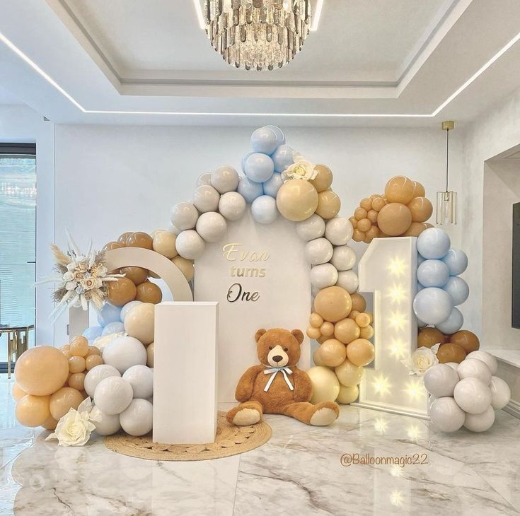 there is a teddy bear sitting in front of the balloon arch and balloons on the wall