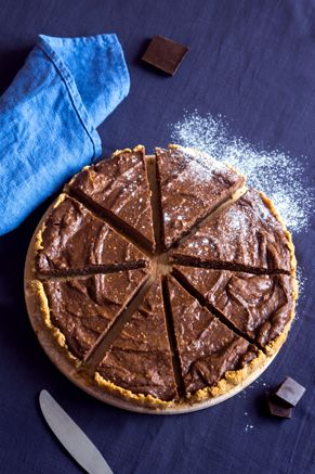 a chocolate pie sitting on top of a table next to a knife and blue napkin