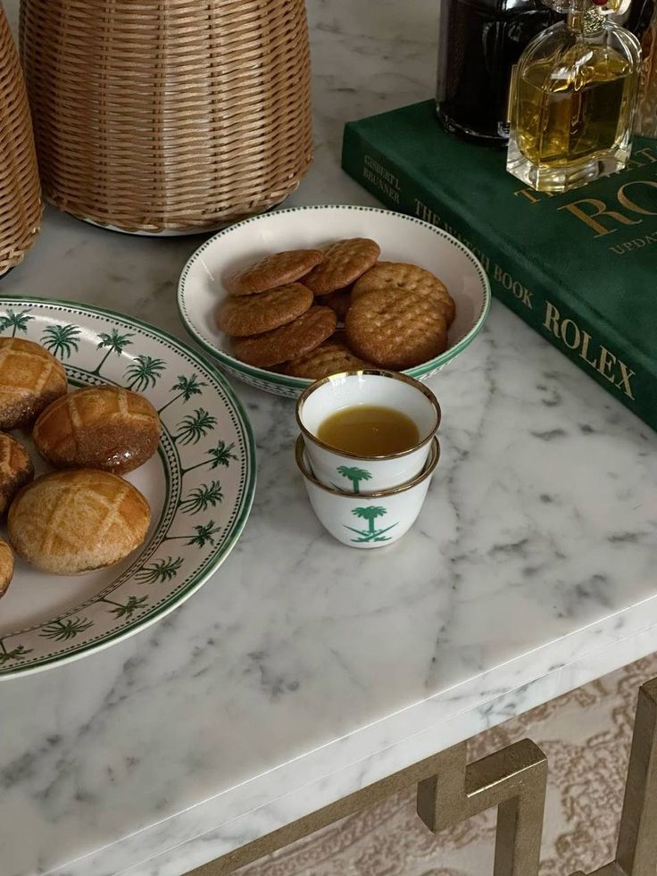 two plates filled with cookies next to a cup and saucer on a marble counter