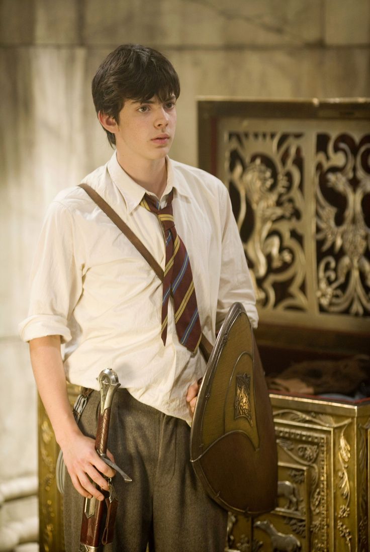 a young man wearing a tie and suspenders standing in front of a gold chest