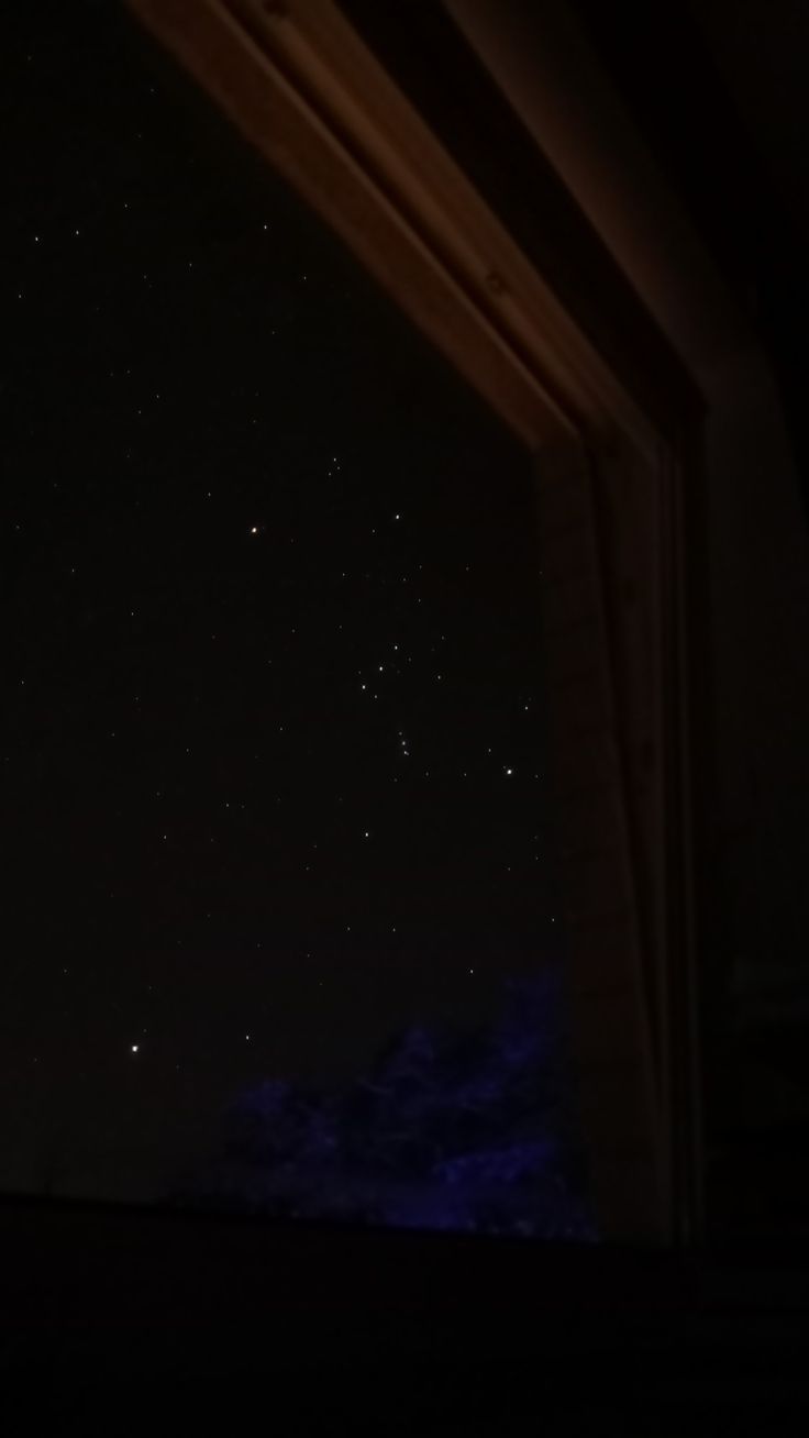 the night sky is lit up with stars in the distance, as seen from an open window