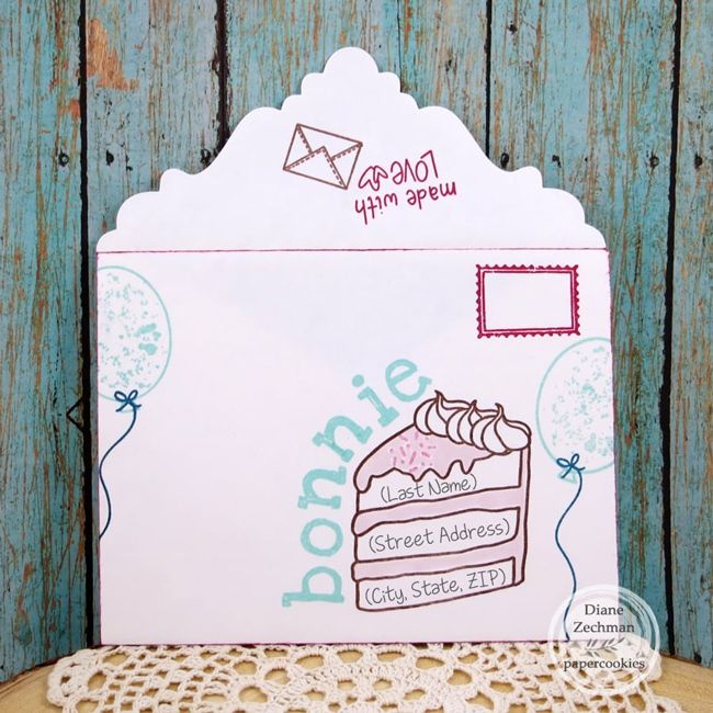 a piece of cake on top of a doily next to a wooden table with an envelope