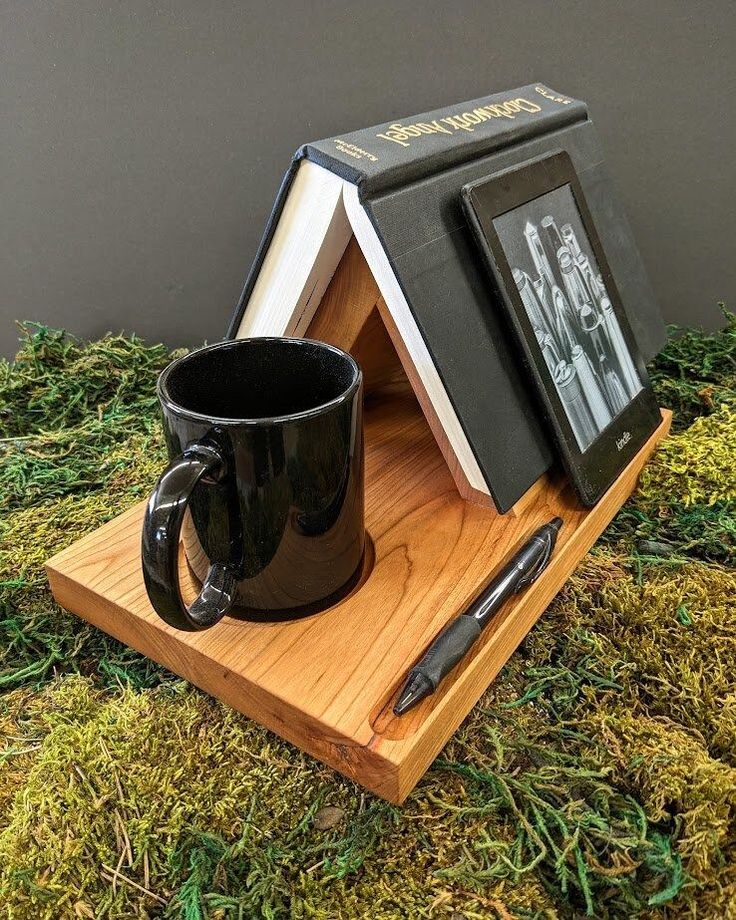 a black coffee mug sitting on top of a wooden stand next to an open book