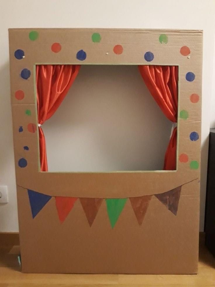 an open cardboard box with red curtains and polka dots on the inside, sitting on a wooden floor