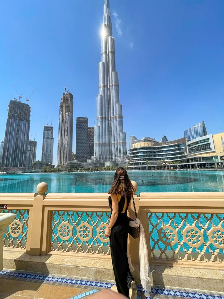 a woman standing in front of the burj tower, looking out over the water