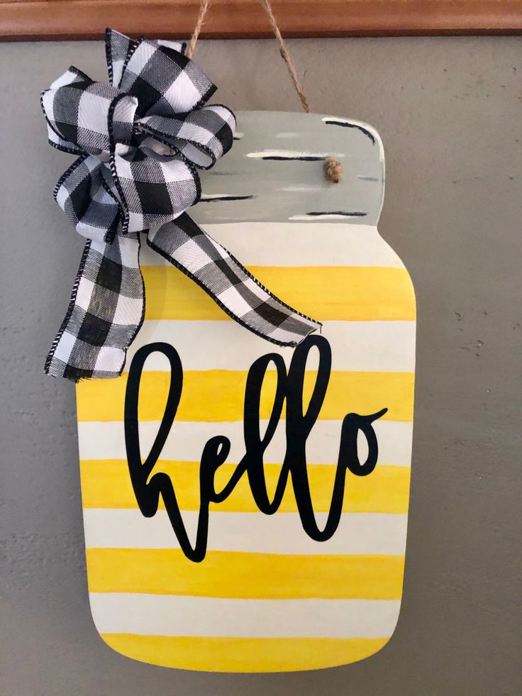 a yellow and white mason jar with the word hello painted on it hanging from a wall