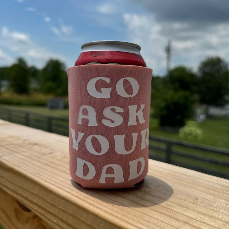 a pink can cooler with the words go ask your dad on it sitting on a wooden deck