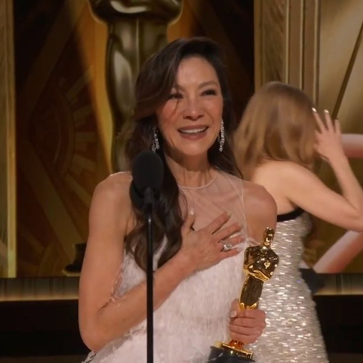 a woman holding an award in front of a screen with her hand on the microphone