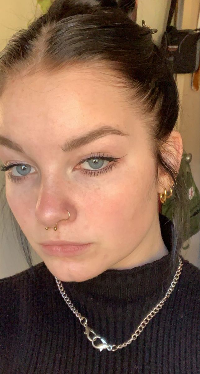 a woman with piercings on her nose wearing a black turtle neck sweater and silver necklace