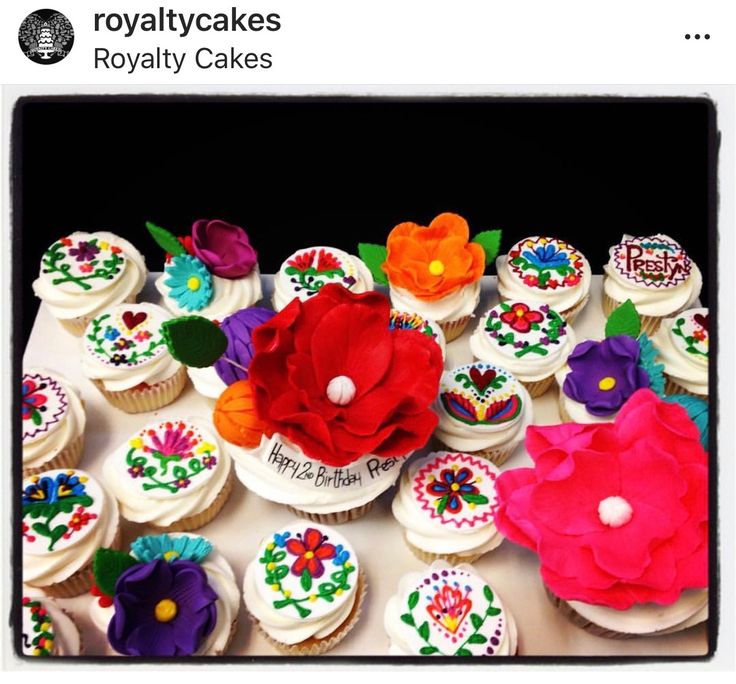 a table topped with lots of cupcakes covered in frosting and colorful flowers