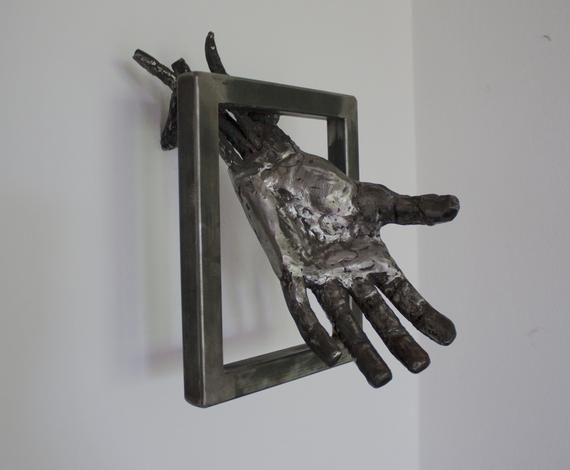 a metal sculpture of a hand hanging on a wall with a square frame attached to it