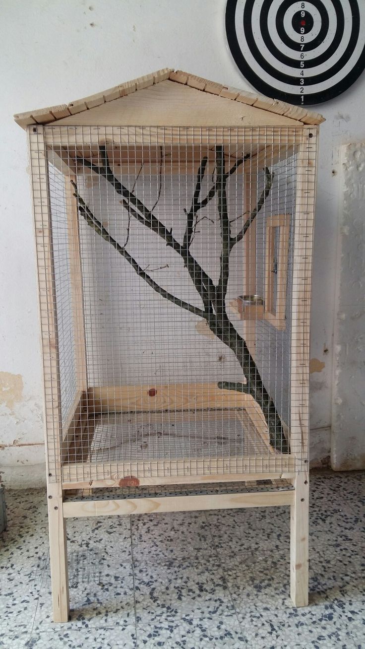 a bird cage with a tree in it and a target on the wall behind it