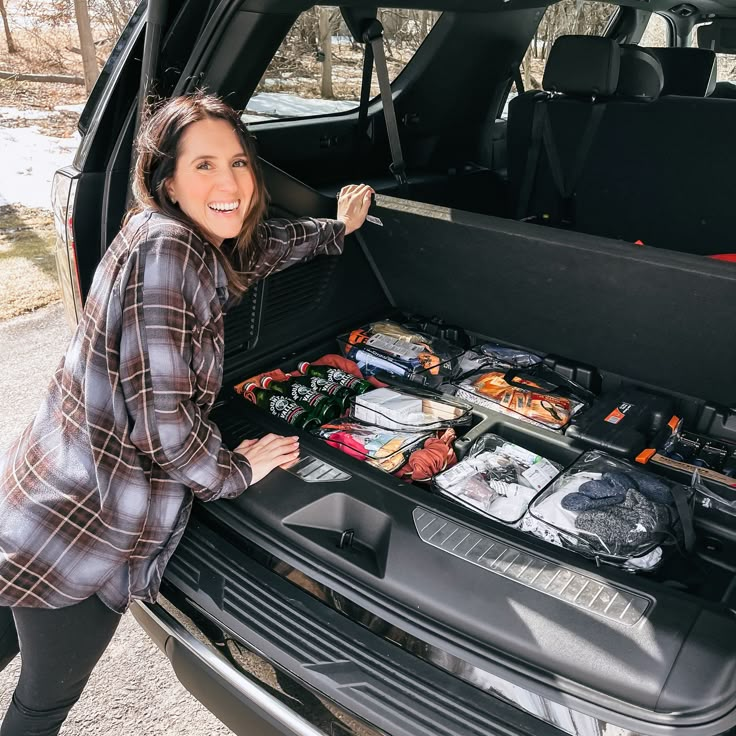 a woman standing next to the trunk of a car filled with food