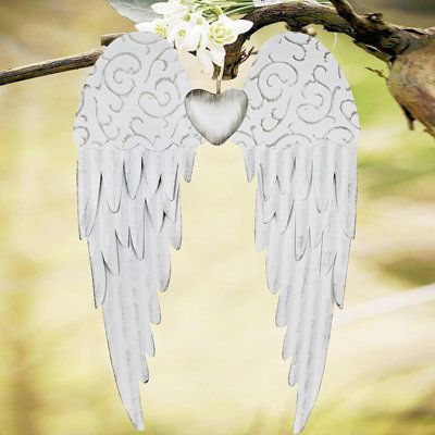 two white angel wings hanging from a tree branch with flowers in the foreground and a bird perched on it's back