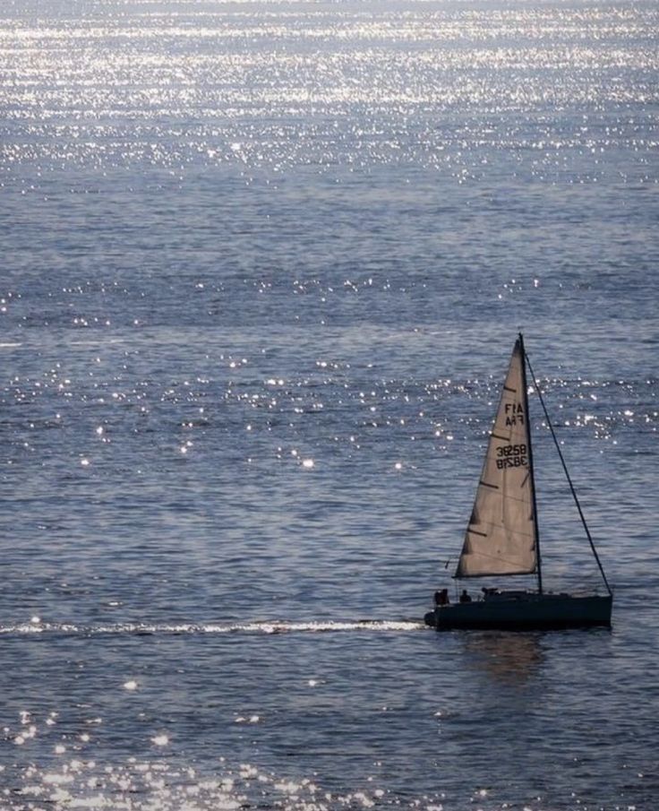 a small sailboat in the middle of an ocean with sun reflecting off the water