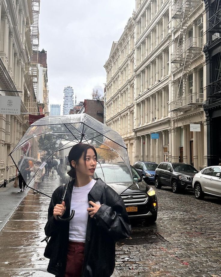 a woman walking down the street with an umbrella in her hand and cars parked on the side walk behind her