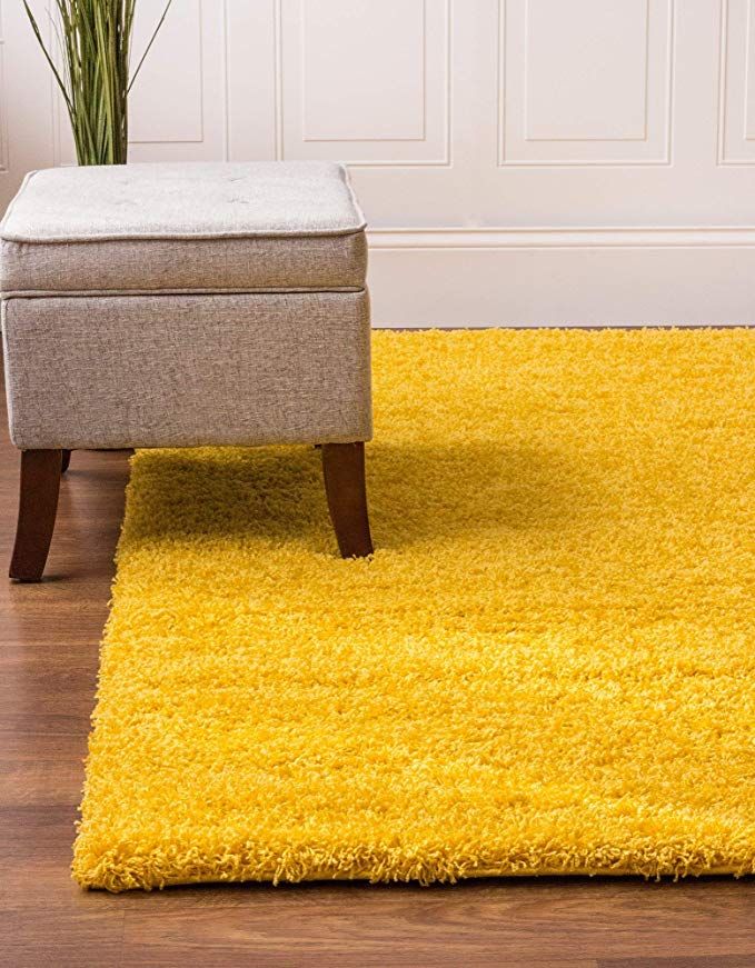 a yellow rug with a footstool in front of it and a potted plant on the floor