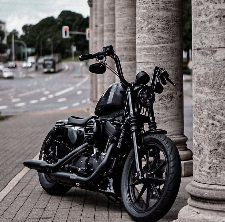 a black motorcycle parked on the side of a road next to tall pillars and columns