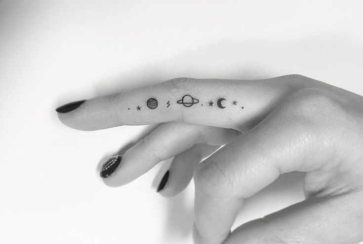 a woman's hand with a small tattoo on the middle finger, and planets