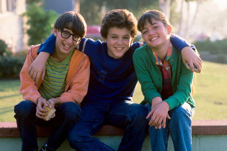 three boys are sitting on a bench and posing for the camera with their arms around each other