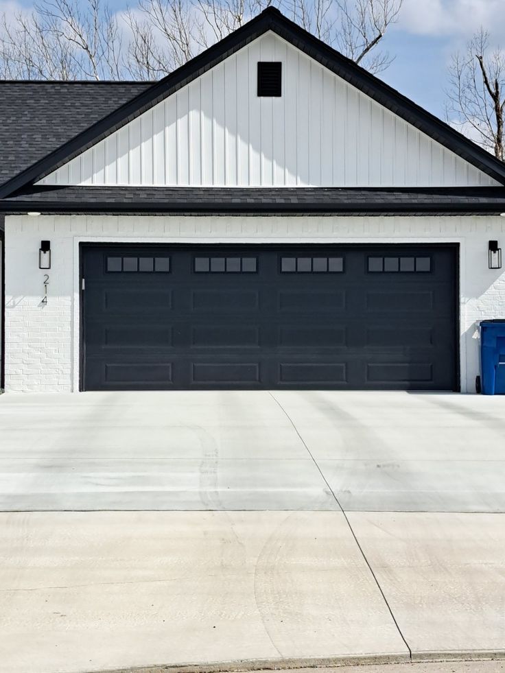 a white house with black roof and two garage doors