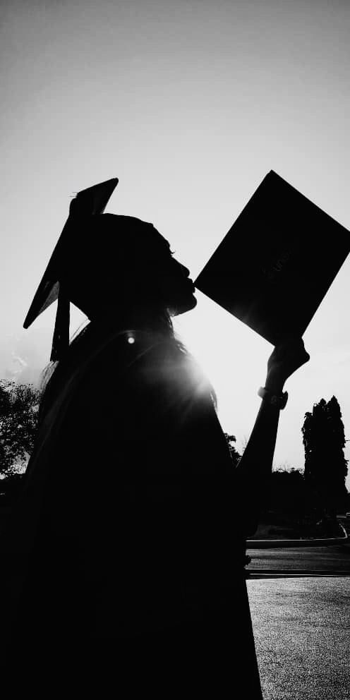 a person with a graduation cap and gown holding a book in their hands while the sun shines behind them