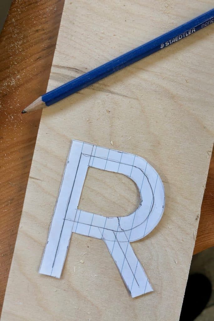 a piece of wood that has been cut into the shape of a letter with a pencil next to it