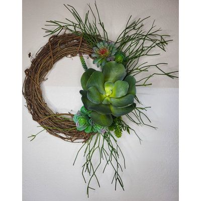 a wreath with succulents and grass hanging on the wall next to a white wall