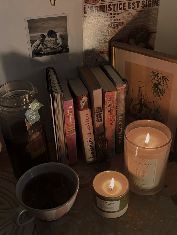 candles and books are on a table next to an open book, coffee cup, and framed photograph