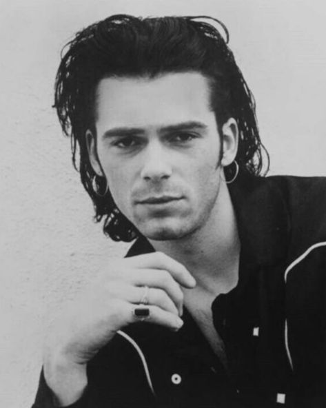 a black and white photo of a man with long hair, wearing a ring on his finger