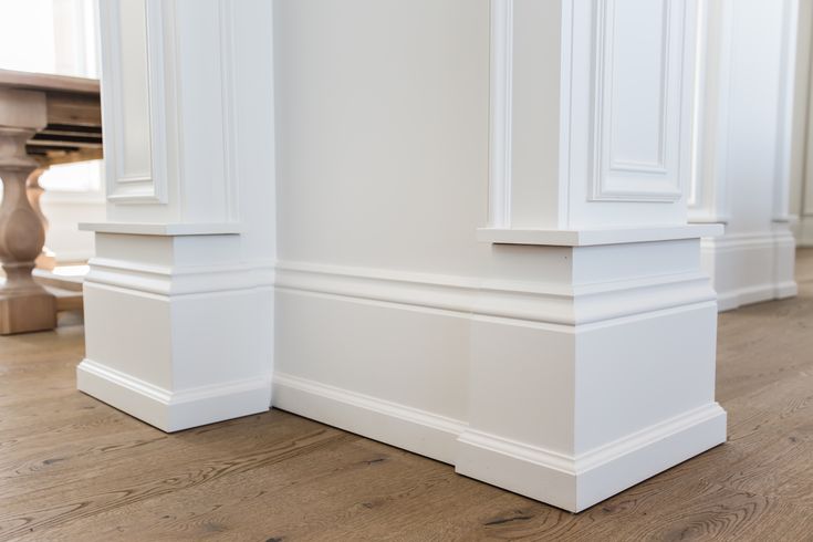 an empty room with white walls and wood flooring on the side, along with two pillars