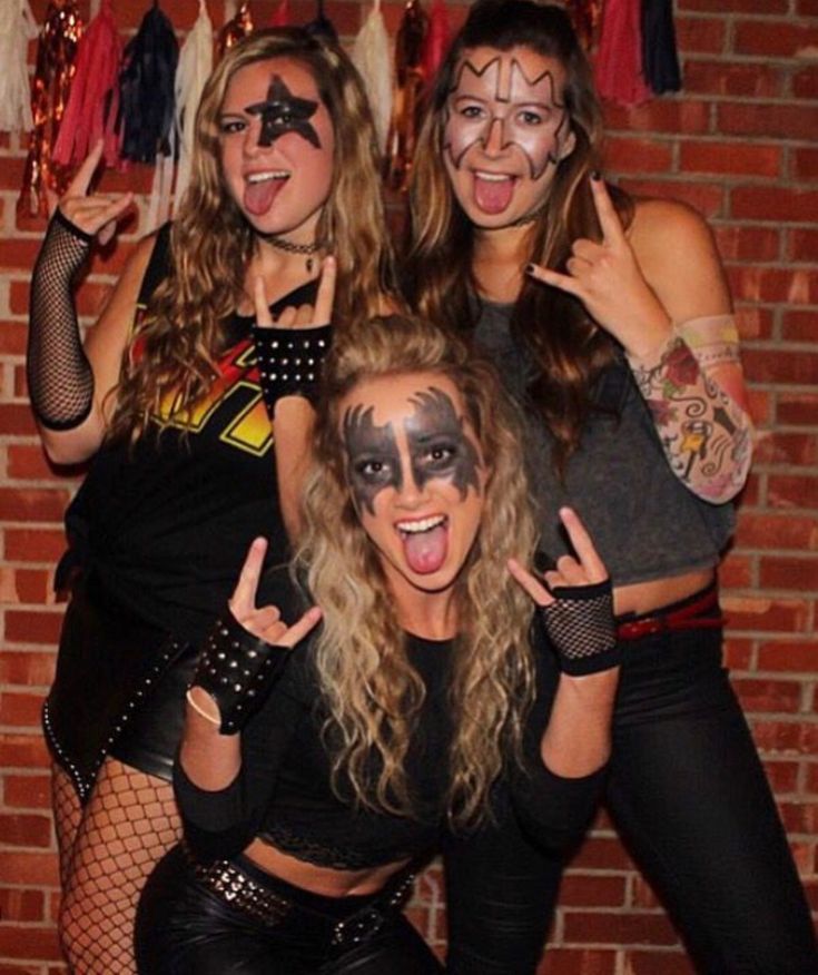 three women with face paint posing for the camera in front of a brick wall and holding their hands up