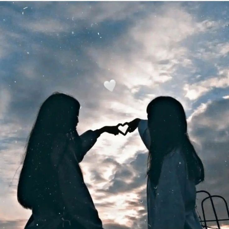 two women standing next to each other with their hands in the shape of a heart