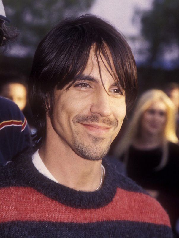 a man with long hair wearing a striped sweater and sunglasses standing next to another man