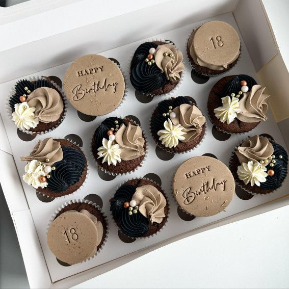 twelve cupcakes with chocolate frosting and flowers in a white box on a table