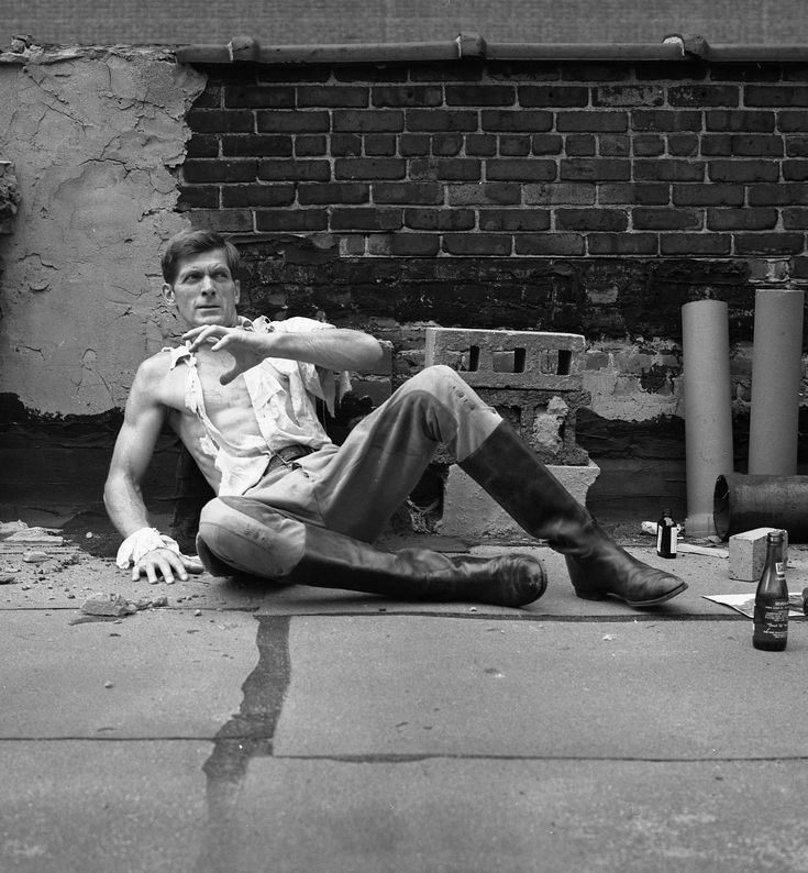 a man sitting on the ground with his legs crossed, leaning against a brick wall