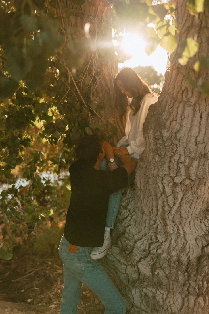 a man and woman leaning up against a tree with the sun shining through the leaves