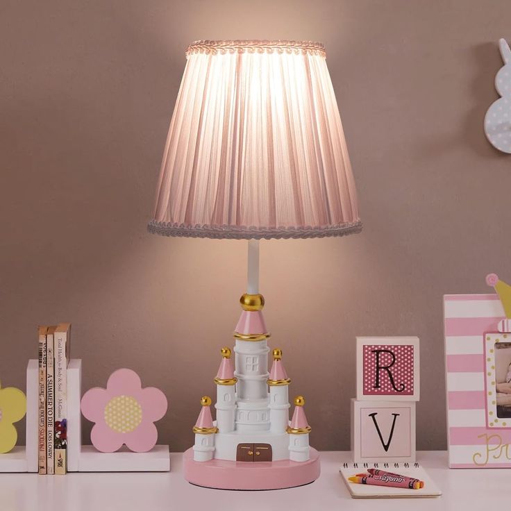 a pink lamp sitting on top of a table next to books and other items in front of a wall