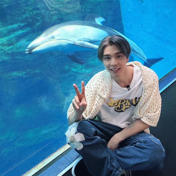 a man sitting in front of a dolphin tank giving the peace sign