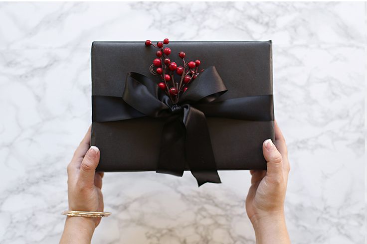 a woman's hands holding up a black gift box with red berries on it