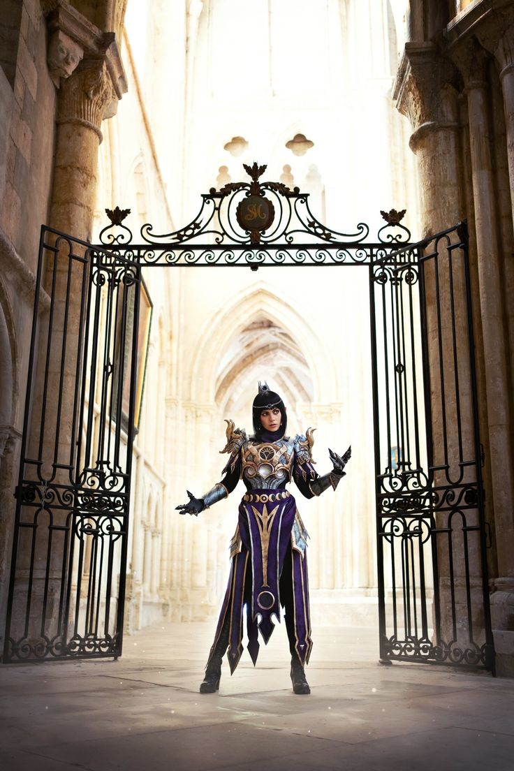 a woman dressed in costume standing under an iron gate