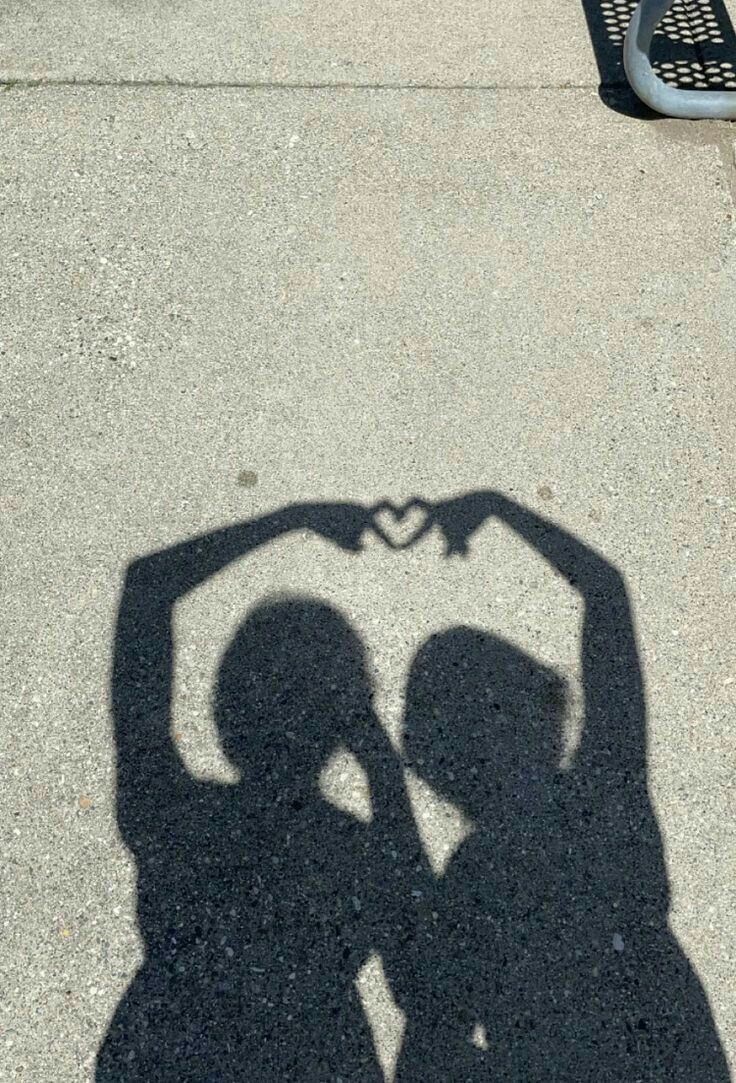 the shadow of two people making a heart shape with their hands on a street curb