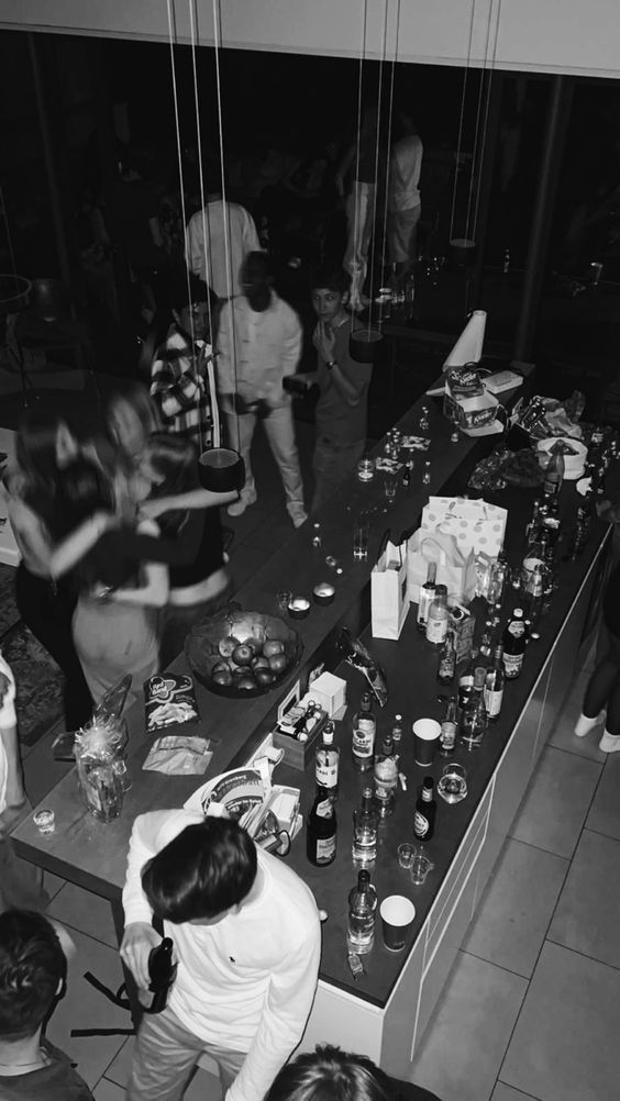 a group of people standing around a table filled with food and drink bottles on it