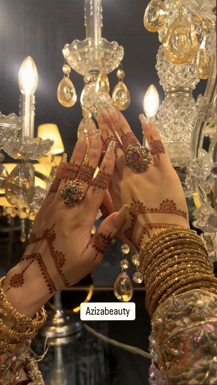 two hands with henna on each hand and chandelier in the back ground