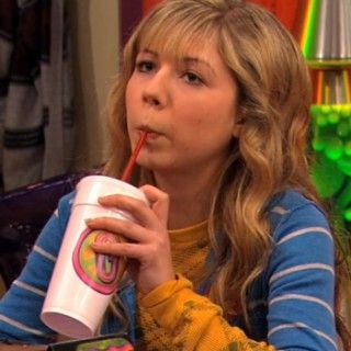 a woman drinking from a cup with a straw in her mouth while sitting at a table