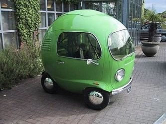 a small green car is parked on the side of the road in front of a building