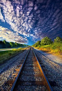 an empty train track with the sky in the background and trees on both sides, under a cloudy blue sky