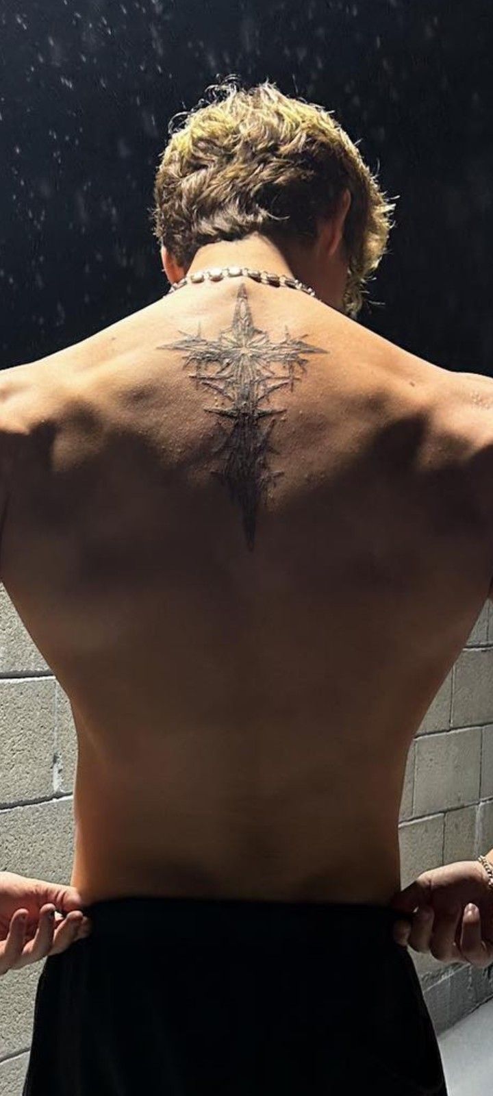 a man with a cross tattoo on his back is standing in front of a mirror