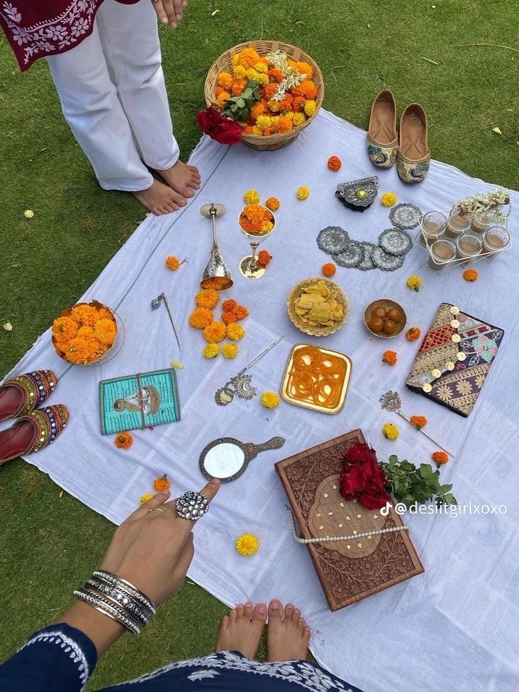 people are sitting at a table with food and flowers on the grass outside in front of them