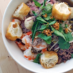 a white bowl filled with meat and veggies on top of a wooden table